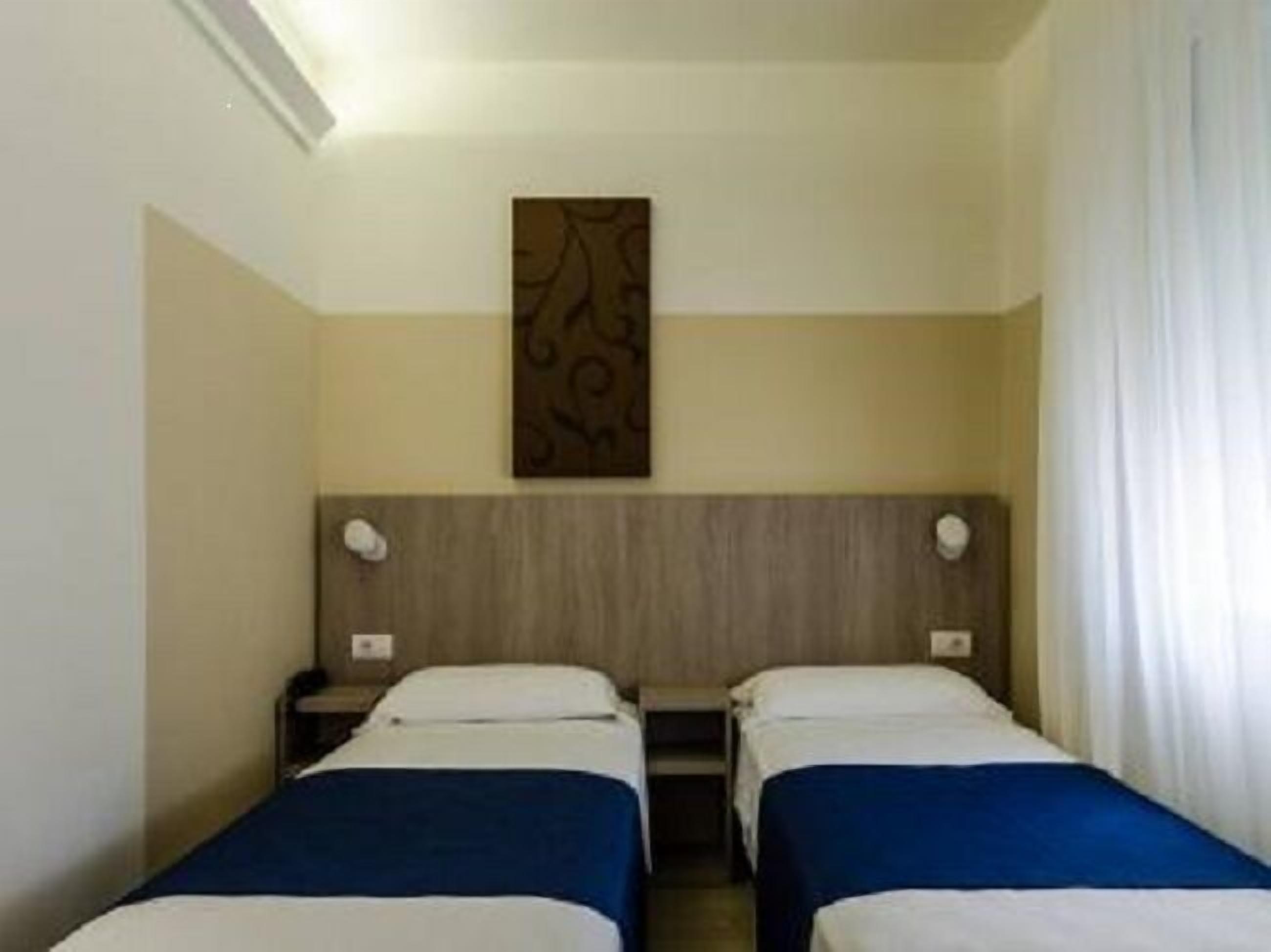 Une chambre d’hôtel avec deux lits simples, une tête de lit en bois, une œuvre d’art accrochée au mur et une table de chevet avec une lampe.