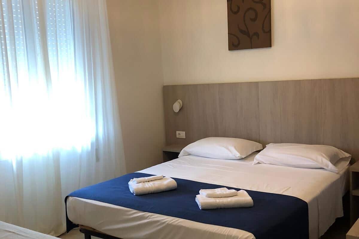 Une chambre d’hôtel comprenant un lit, des tables de chevet, un banc, un luminaire suspendu et une œuvre d’art murale.