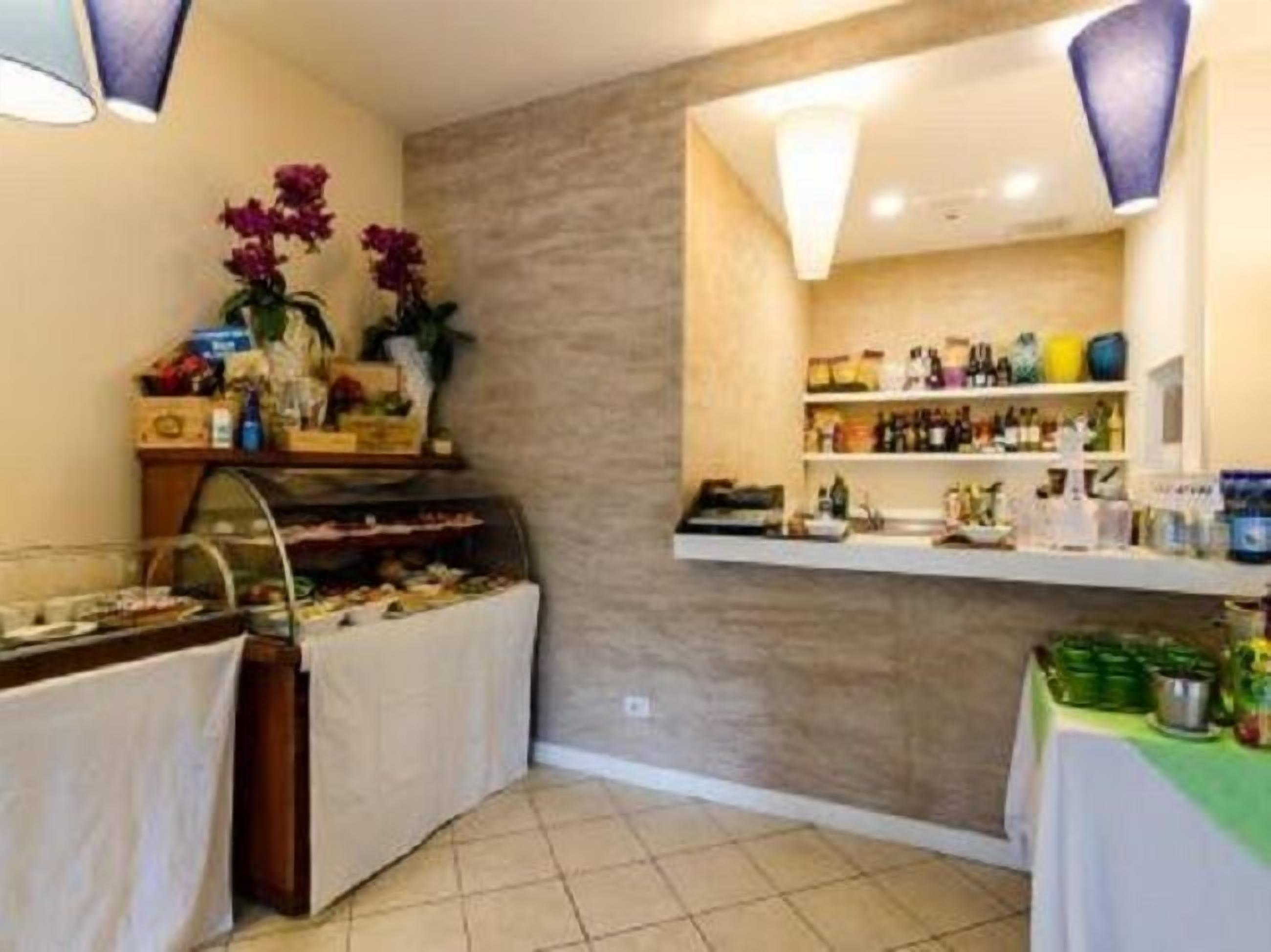 Zona de bufé con diversos alimentos, una vitrina con flores y un estante con bebidas.