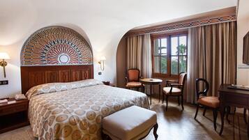 Una habitación de hotel con una cama grande, un escritorio, dos sillas, una mesita y un panel decorativo en la pared.