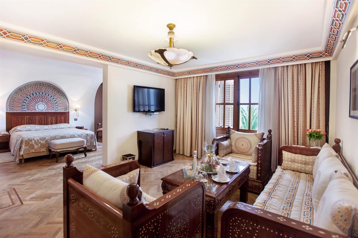 A hotel room with a large bed, a sofa, a TV, and a decorative ceiling.