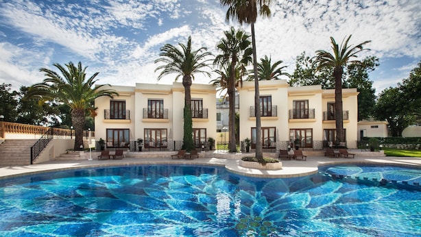 Ein Swimmingpool mit blauem Mosaikdekor, umgeben von Palmen und einem Gebäude mit Balkonen.
