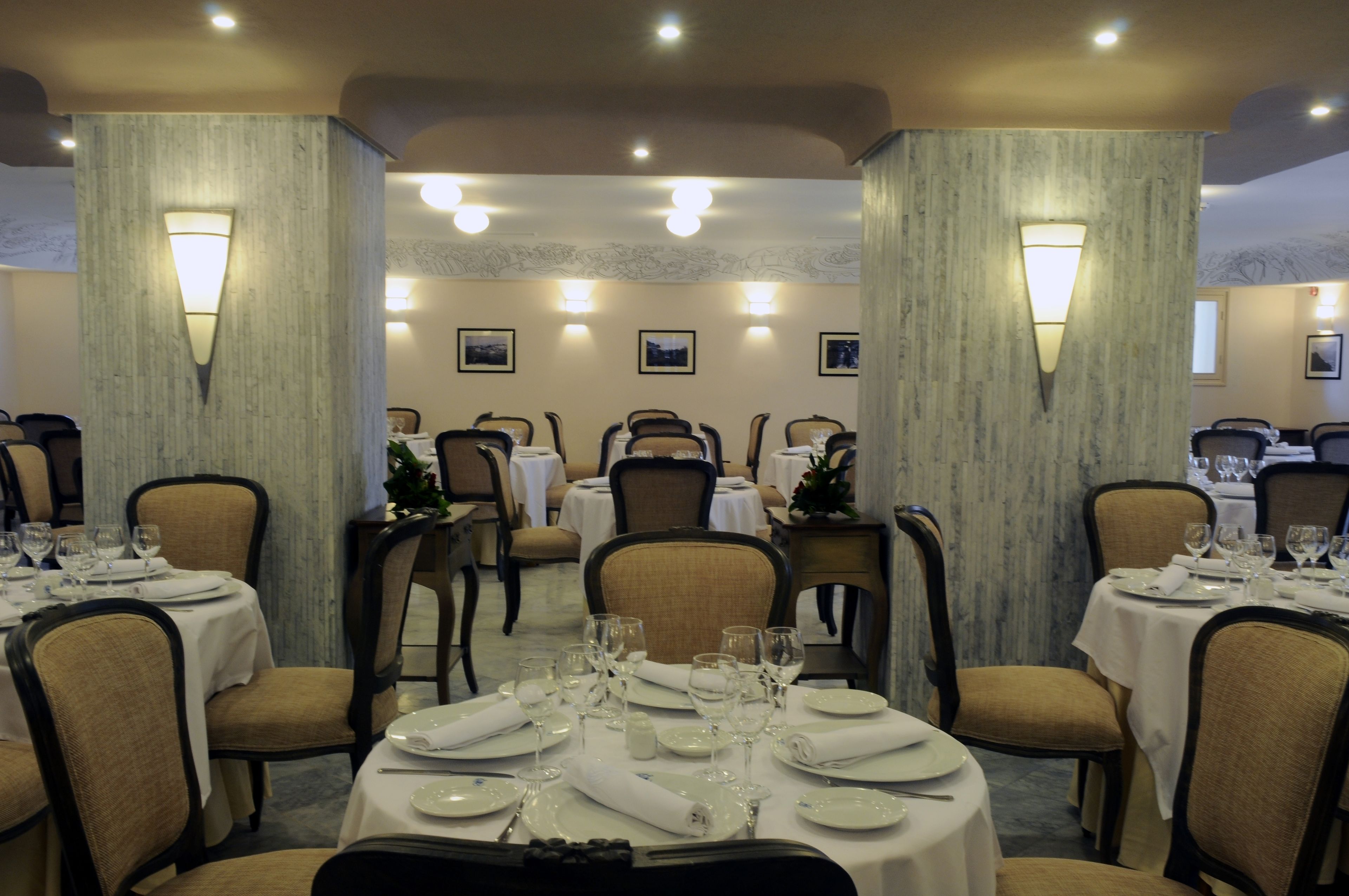 A dining area with round tables set for four, each with white tablecloths, chairs, and glassware.