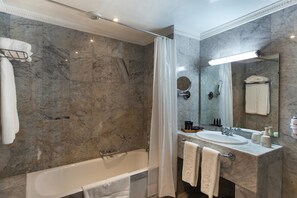 Une salle de bain moderne avec un mur en marbre, une baignoire, un lavabo avec des articles de toilette et un miroir.