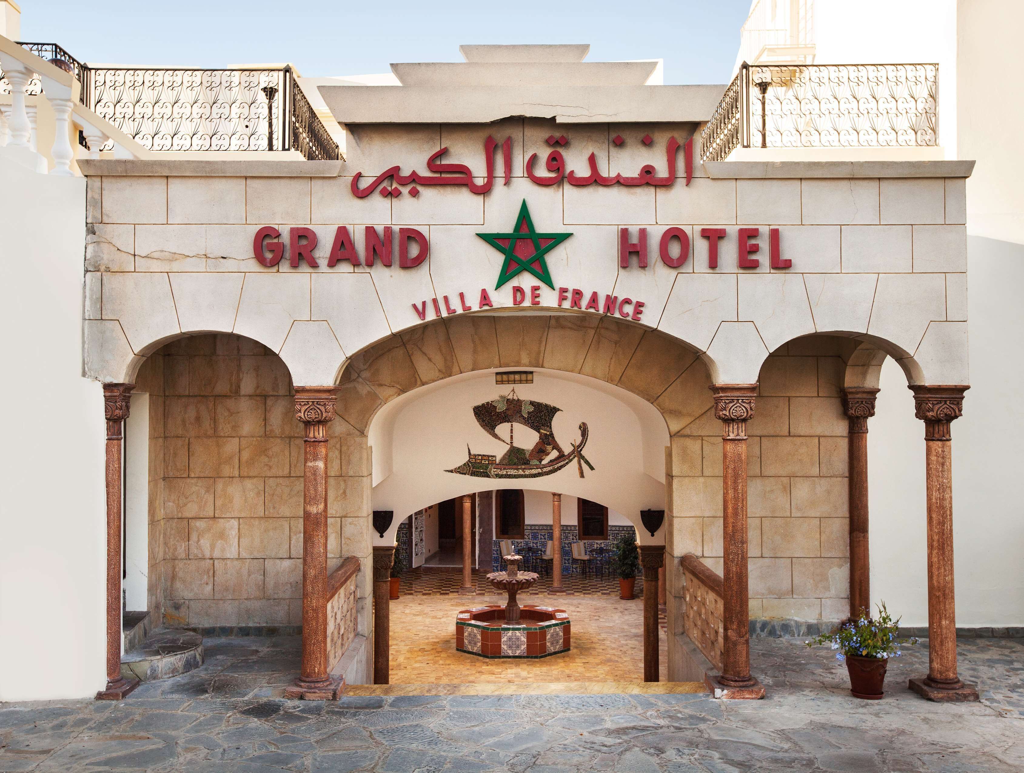 The entrance of the Grand Hotel with a sign in Arabic and French, featuring a star emblem and a horse statue.