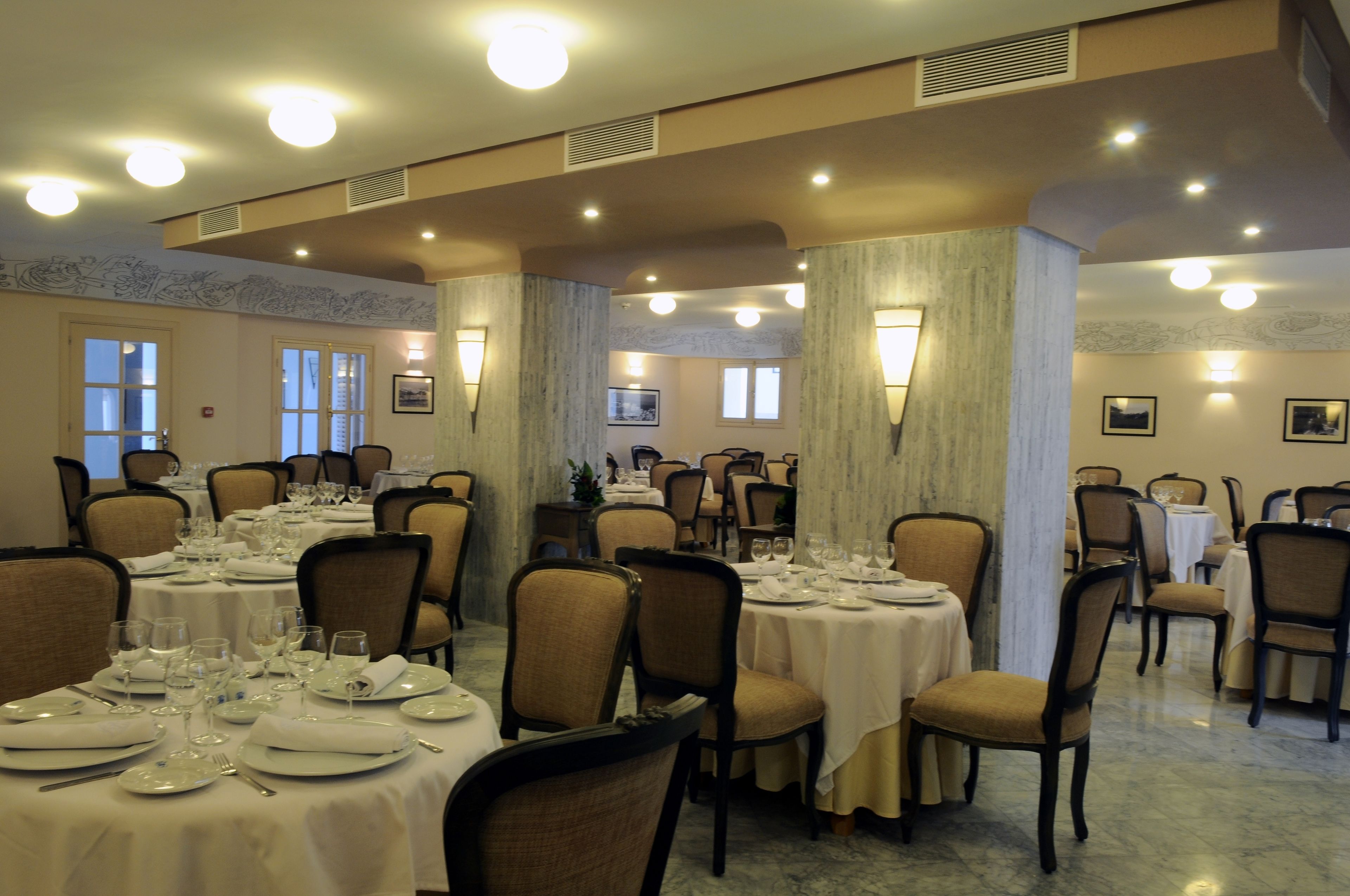 Un espace repas avec plusieurs tables dressées pour le service, où les chaises et les tables sont recouvertes de nappes blanches.