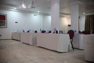 Un salón de conferencias con varias mesas, cada una cubierta con un mantel blanco y equipada con botellas de agua y sillas rojas.
