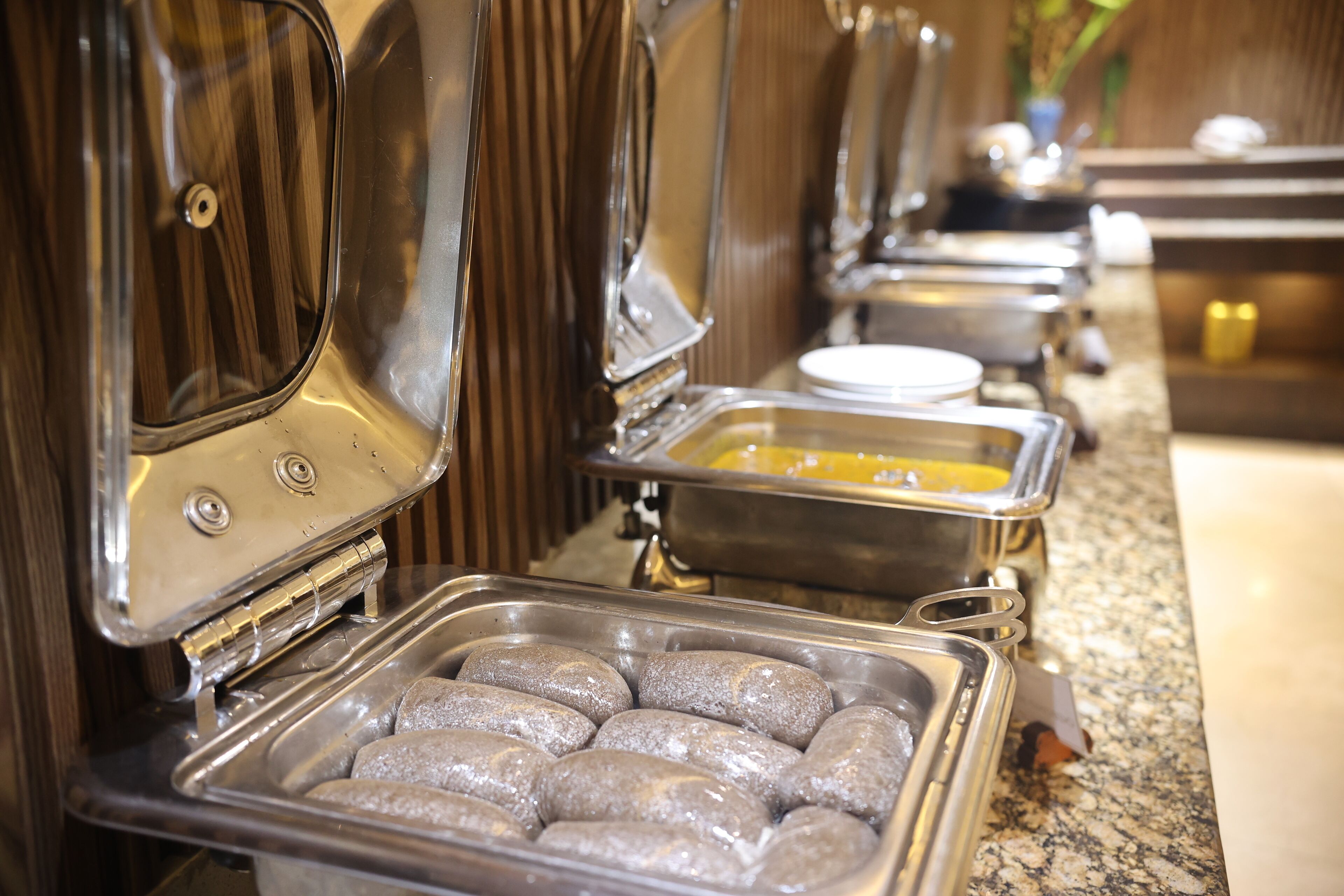 Un buffet avec différents plats présentés dans des récipients variés et accompagné d’ustensiles.
