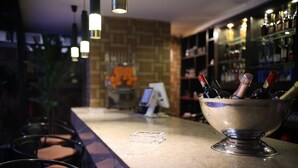 Un espace bar avec un comptoir, des tabourets de bar, un présentoir de bouteilles et un mur de briques agrémenté d’un élément décoratif en arrière-plan.
