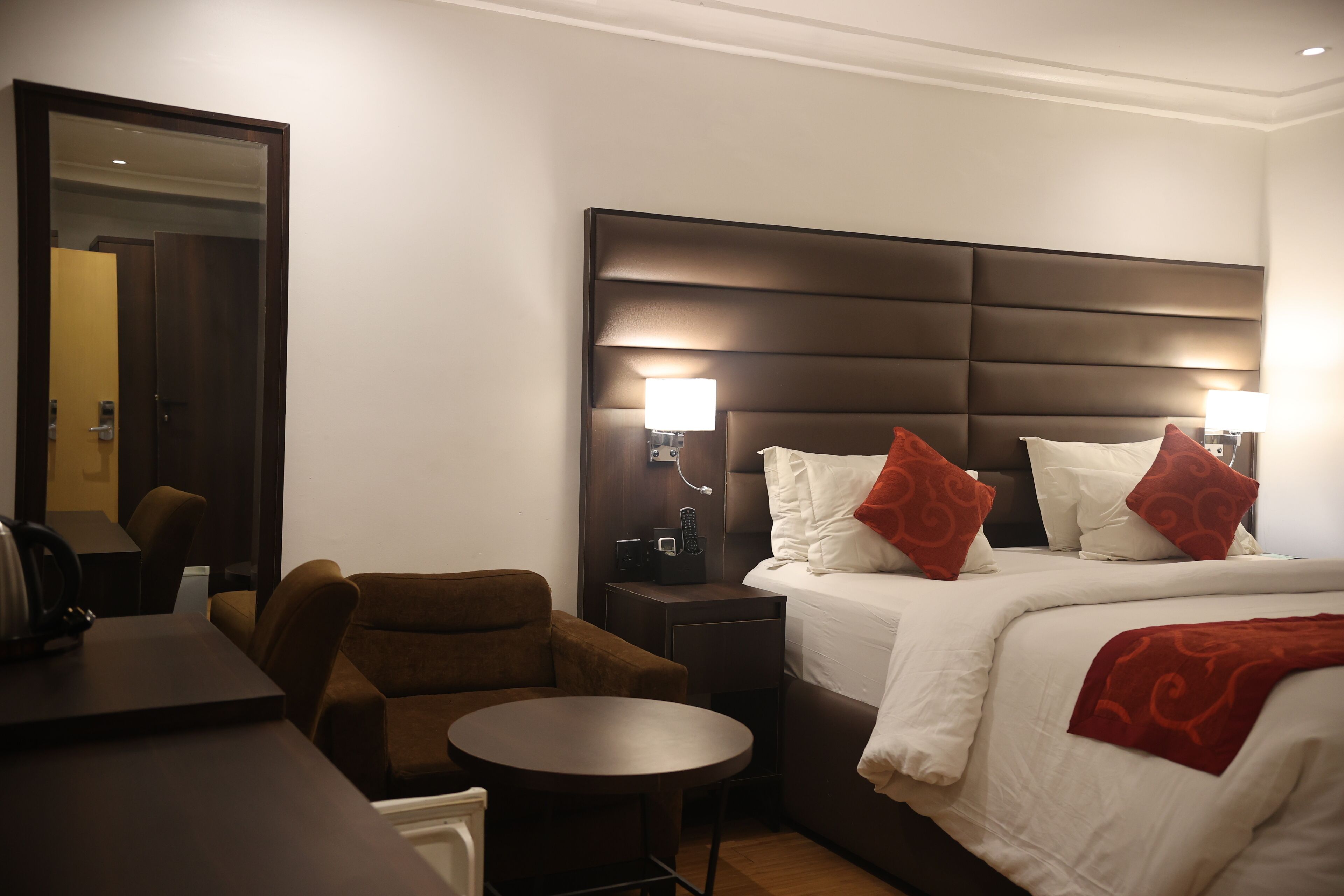 A hotel room with a bed, bedside table, lamp, chair, and a small round table.