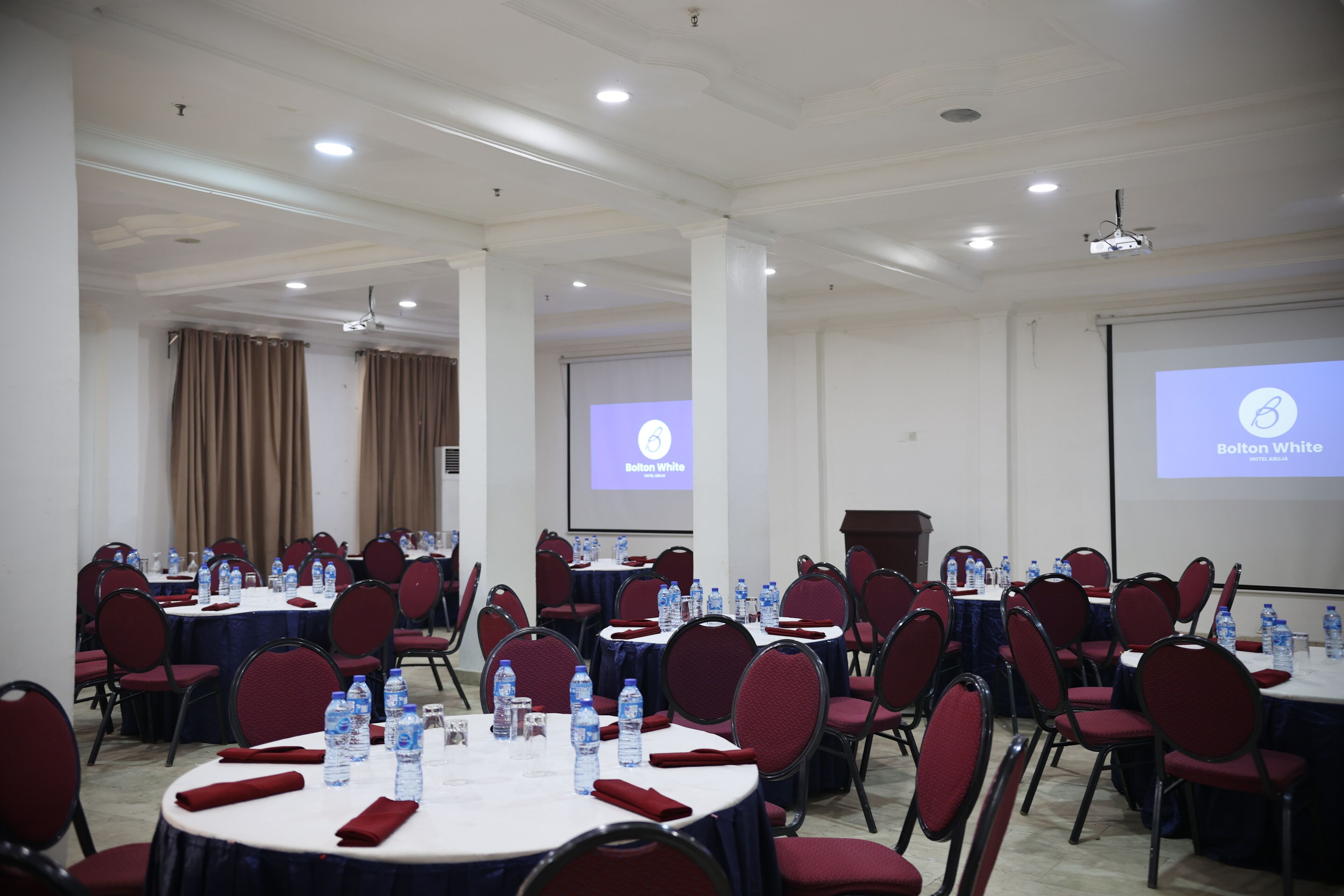 A conference room with round tables, red chairs, and water bottles.