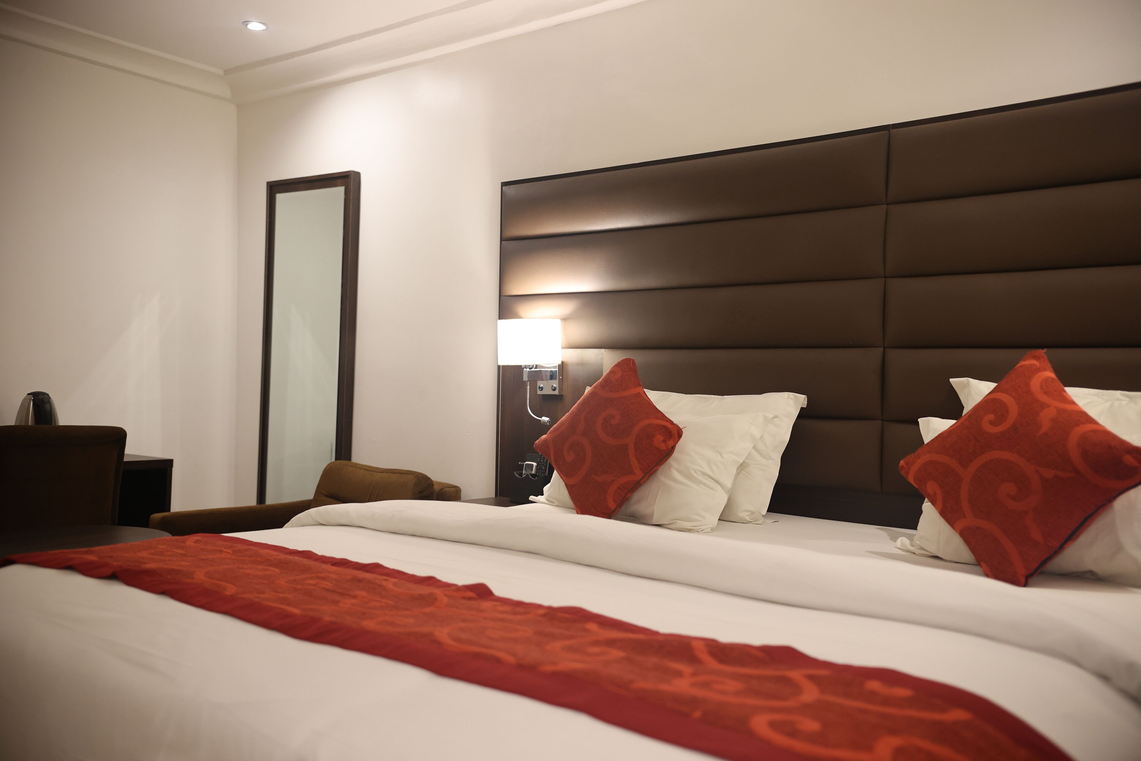 A hotel room with a large bed, a nightstand, a lamp, and a mirror.