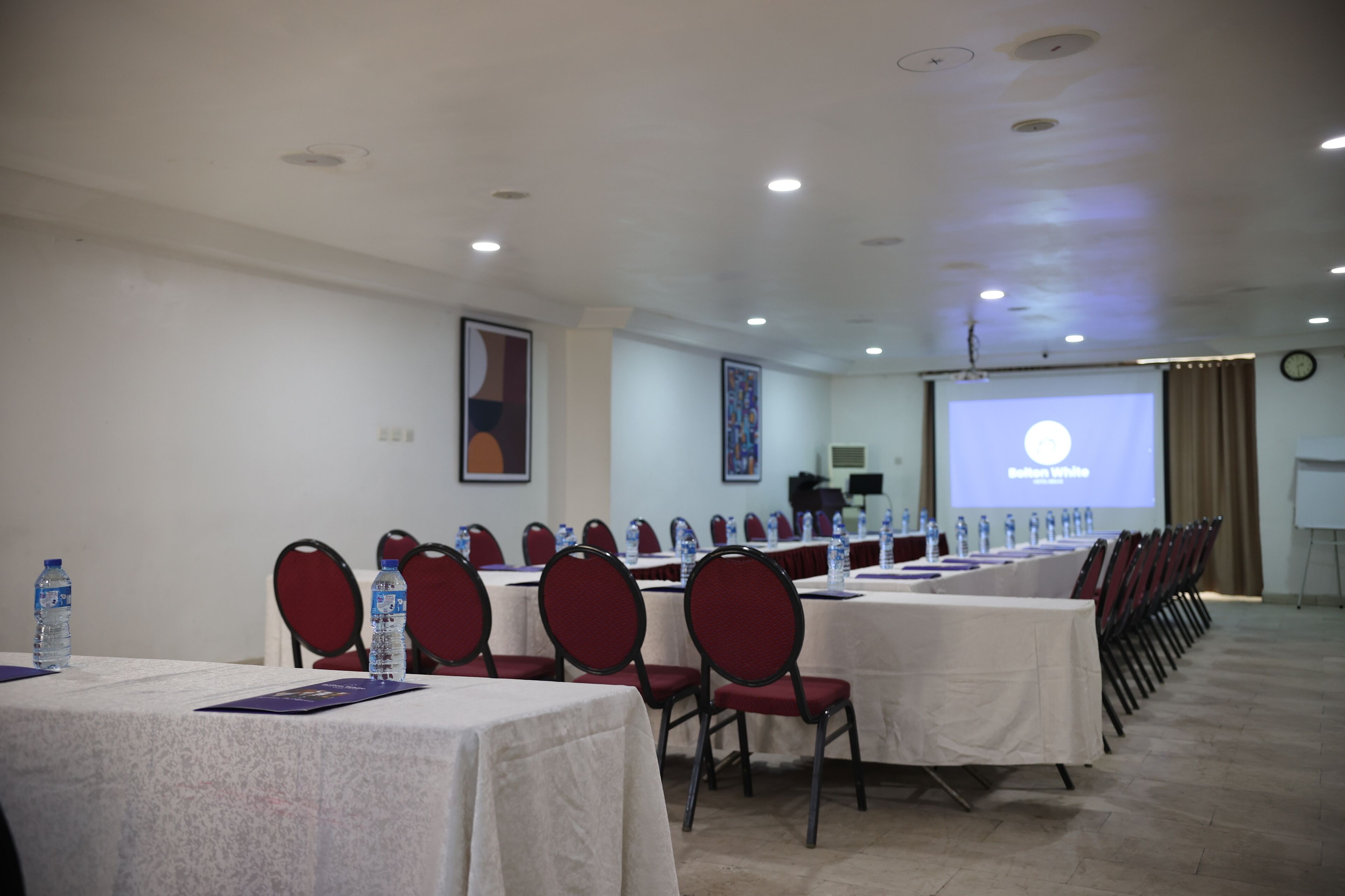 Une salle de conférence équipée de tables et de chaises, d’un écran de projection et de bouteilles d’eau posées sur les tables.