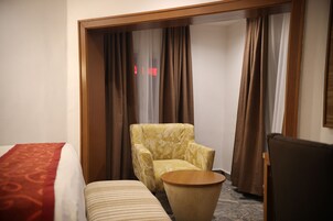 A hotel room with a bed, a chair, a small table, and a wardrobe with curtains.