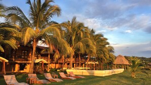 A resort with palm trees, lounge chairs, and a thatched-roof structure. - Hotel El Sitio Playa Venao (Las Escobas del Venado)