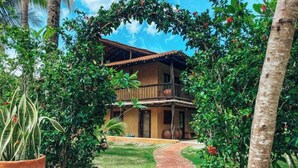A two-story building with a brick pathway leading to the entrance, surrounded by lush greenery and palm trees. - Hotel El Sitio Playa Venao (Las Escobas del Venado)