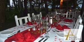 Mesa dispuesta para una comida con sillas blancas, servilletas rojas y copas de cristal.