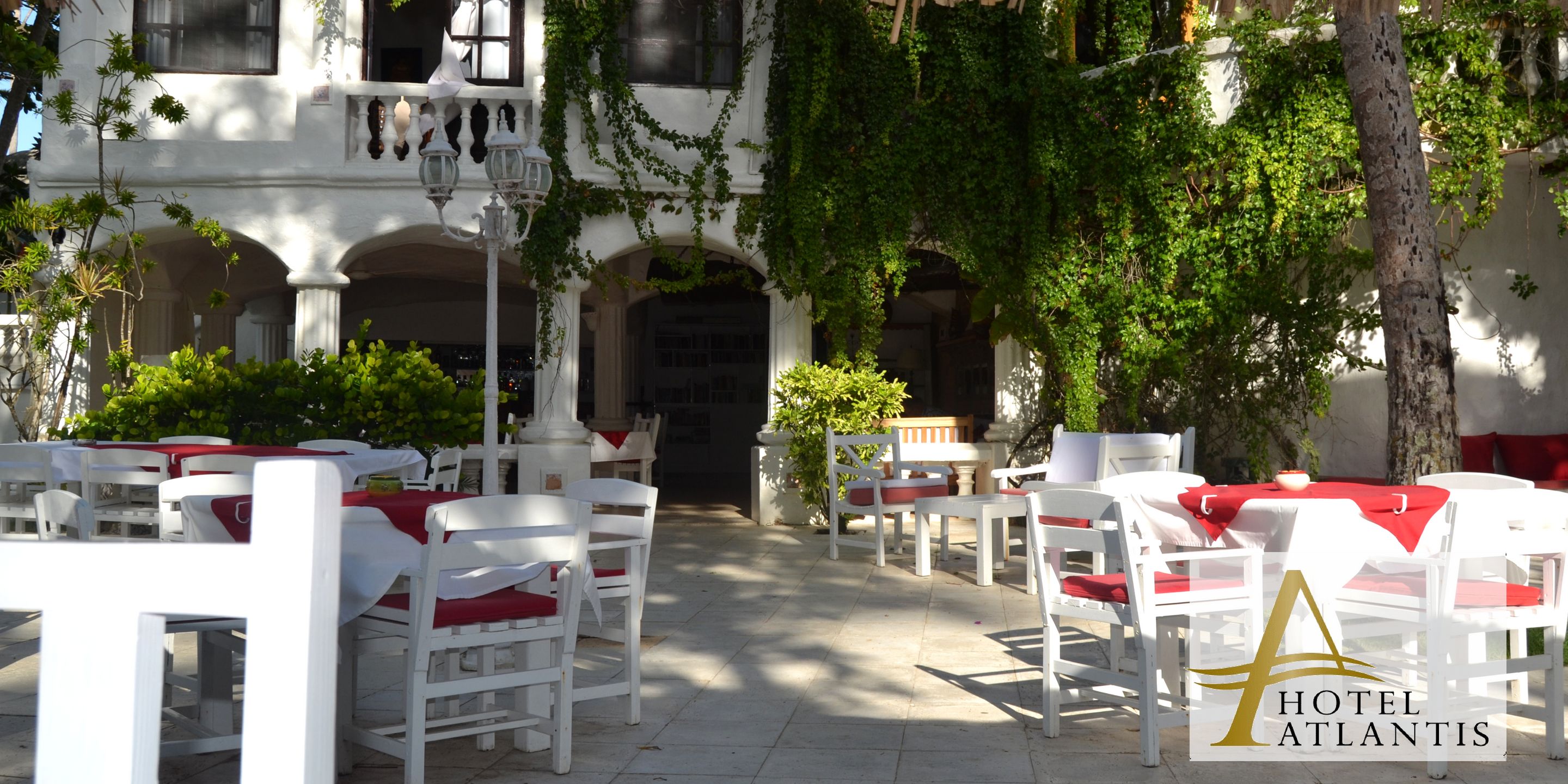 Un patio de hotel con mesas y sillas blancas, una fuente y un edificio con arcos e hiedra.