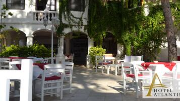Un patio de hotel con mesas y sillas blancas, una fuente y un edificio con arcos e hiedra.