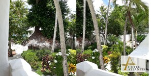 Un exuberante jardín con palmeras, una estructura de techo de paja y un edificio blanco con un logotipo.