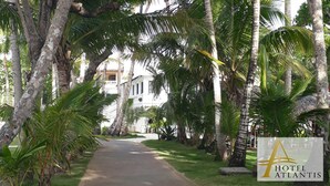 A pathway lined with palm trees leading to a white building with a balcony. - Hotel Atlantis (Las Terrenas)
