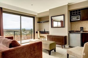 A modern living room with a sofa, a coffee table, and a dining area with a chair and a small table. There is a kitchen area with a microwave and a refrigerator. - Auberge Du Vin, Tupungato, Mendoza (Tupungato)