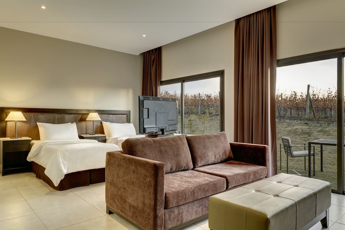 A hotel room with a bed, a sofa, a TV, and a large window with a view of the outdoors.