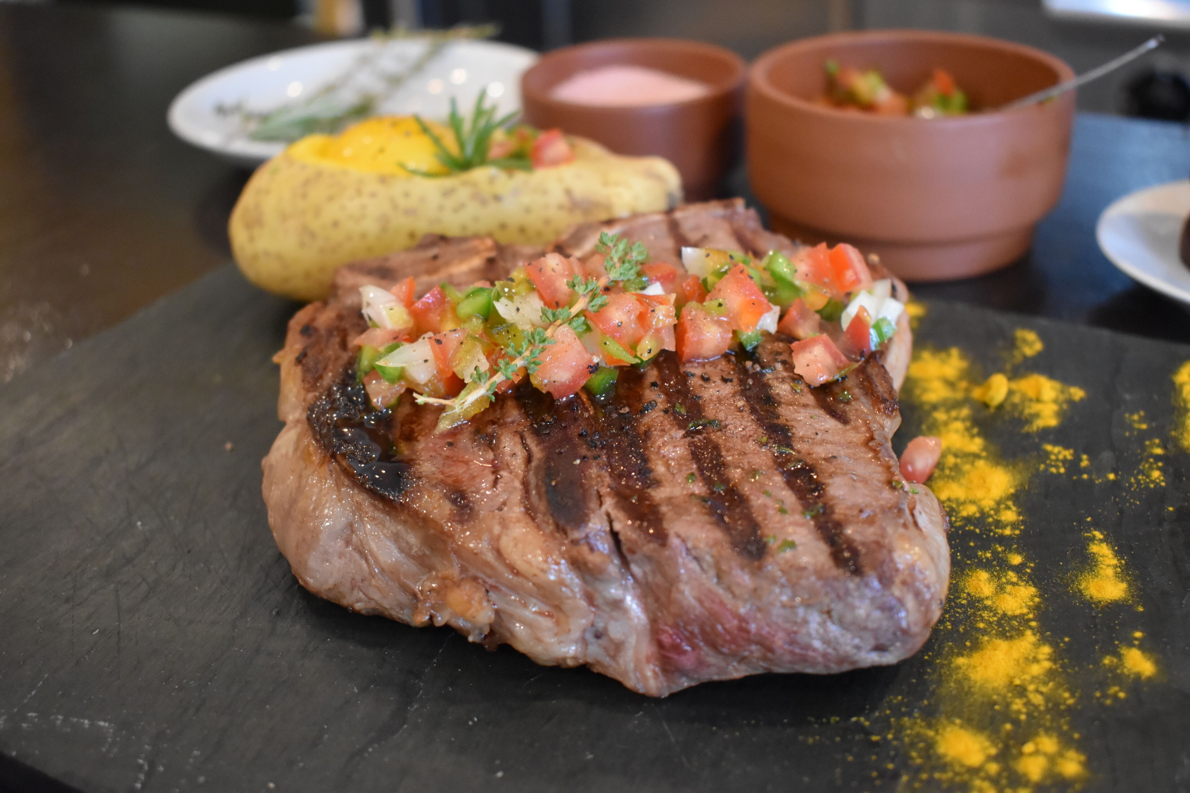 Ein Steak mit Grillstreifen und Tomatenbelag auf einer schwarzen Platte.