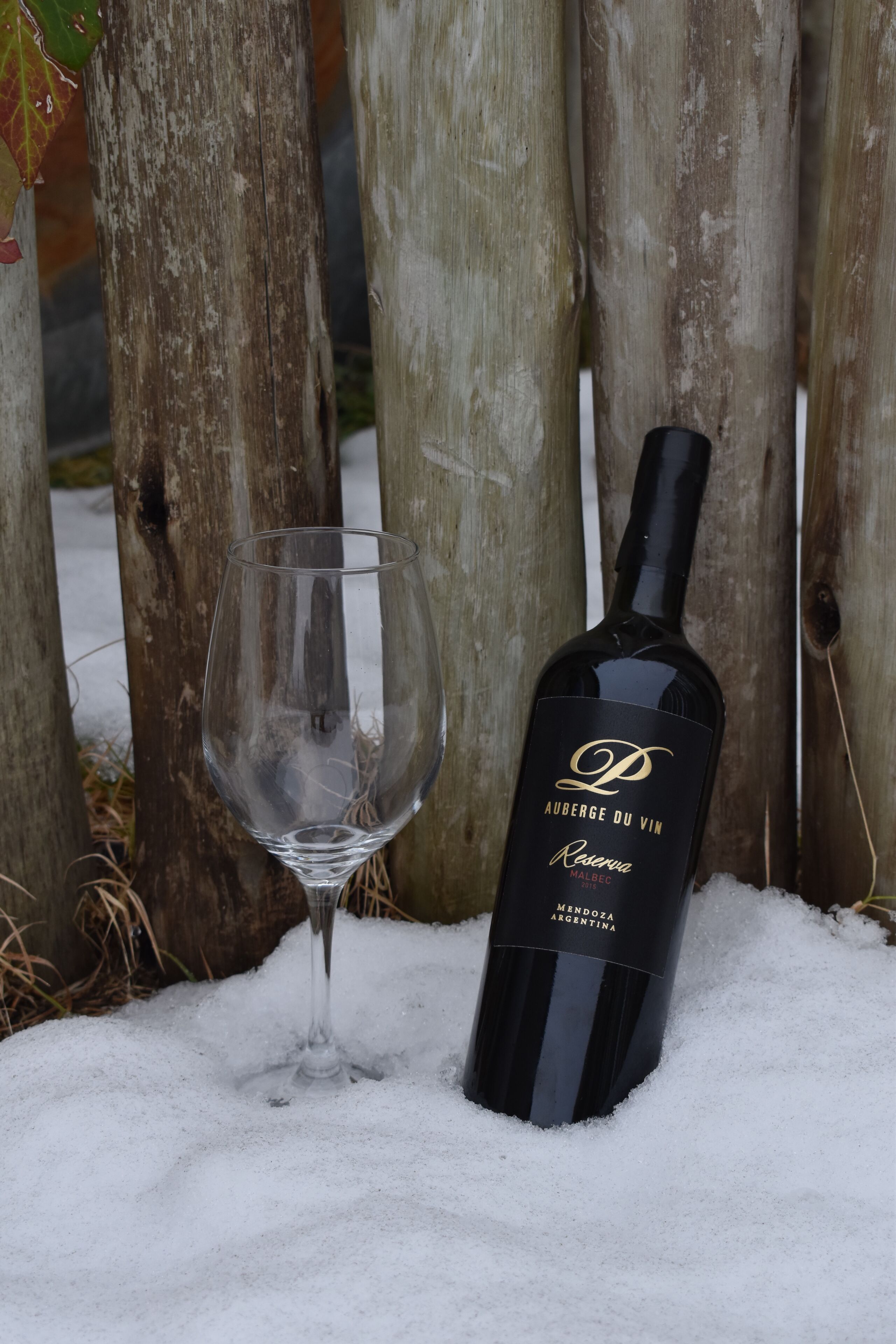A bottle of wine and an empty glass on a snowy surface.