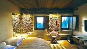 A bedroom with a stone wall, a bed, a desk, and a window with a view. - Castello di Montalbano (Florence)