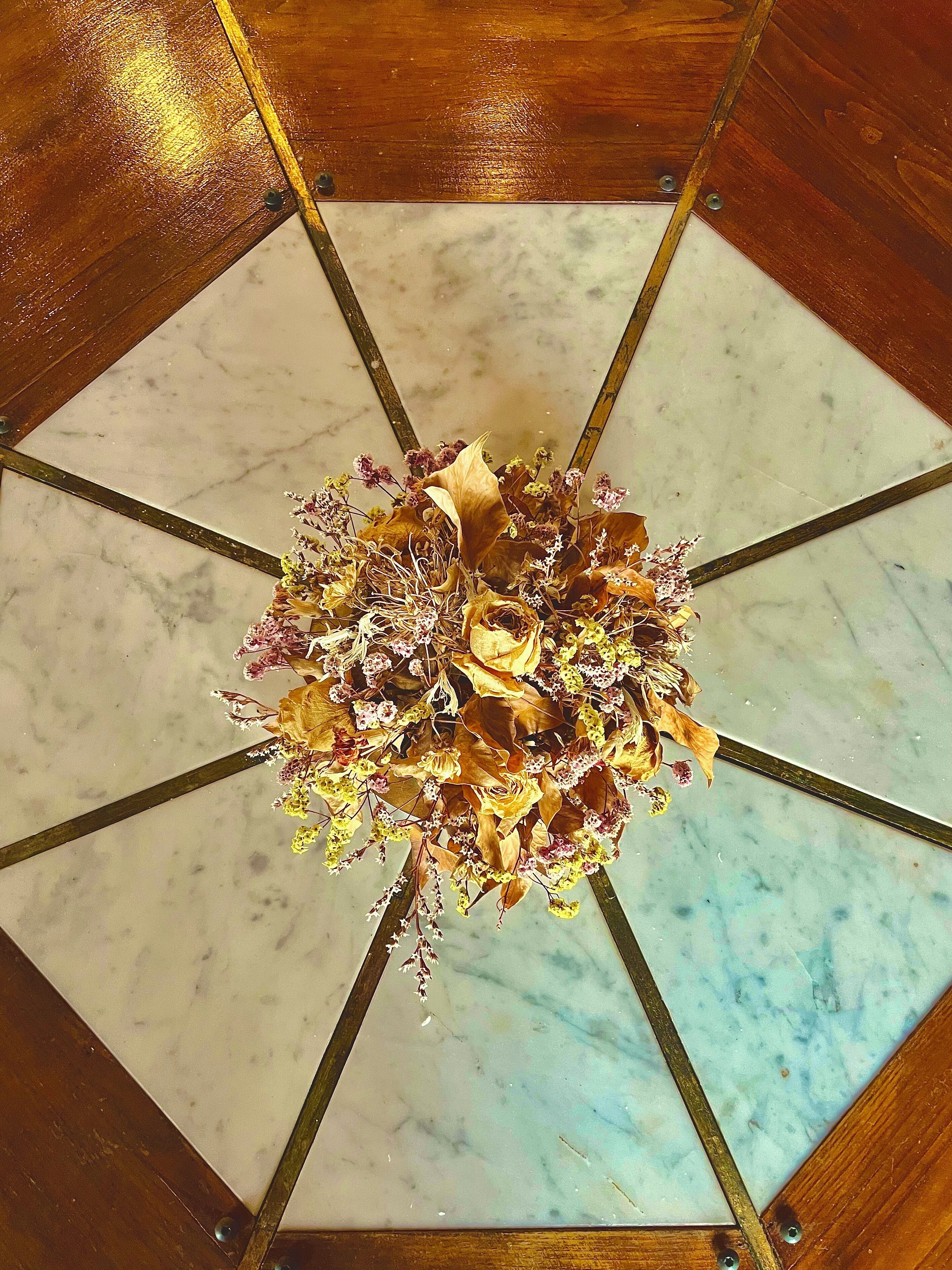 A chandelier with a floral arrangement in a square room with a marble floor and wooden beams.
