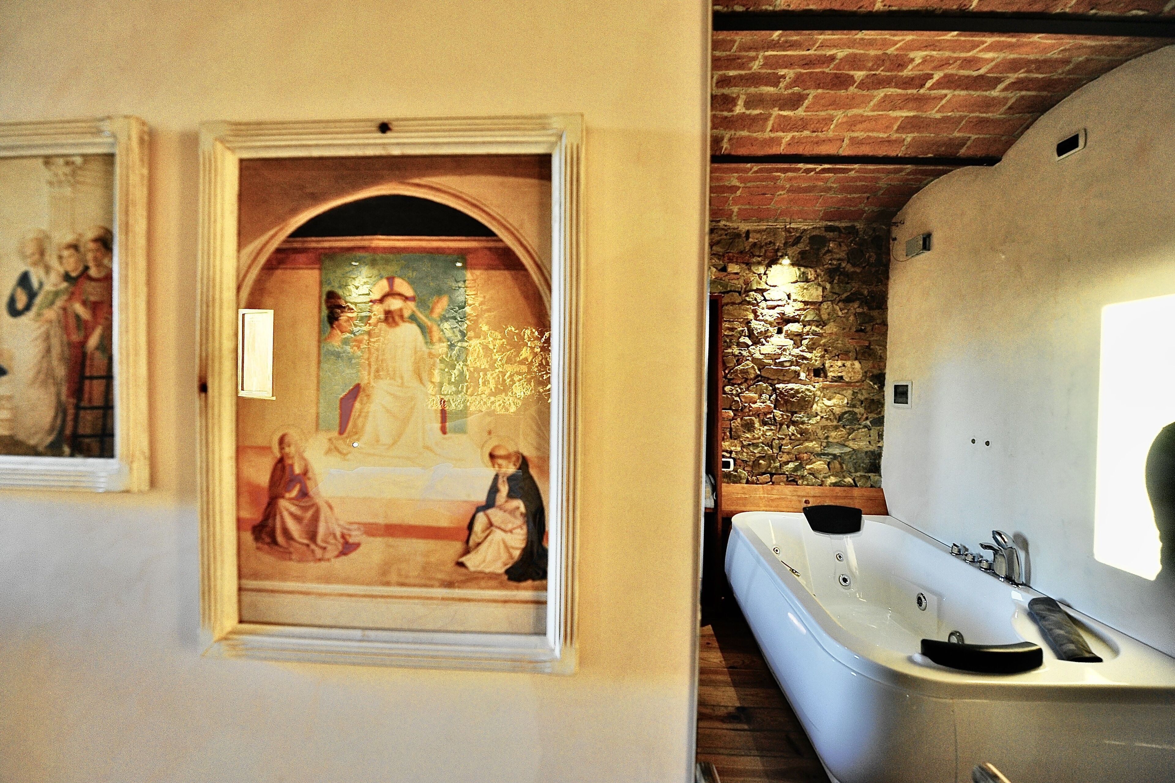 Une salle de bain avec une baignoire blanche, un mur en pierre et un tableau encadré accroché au mur.