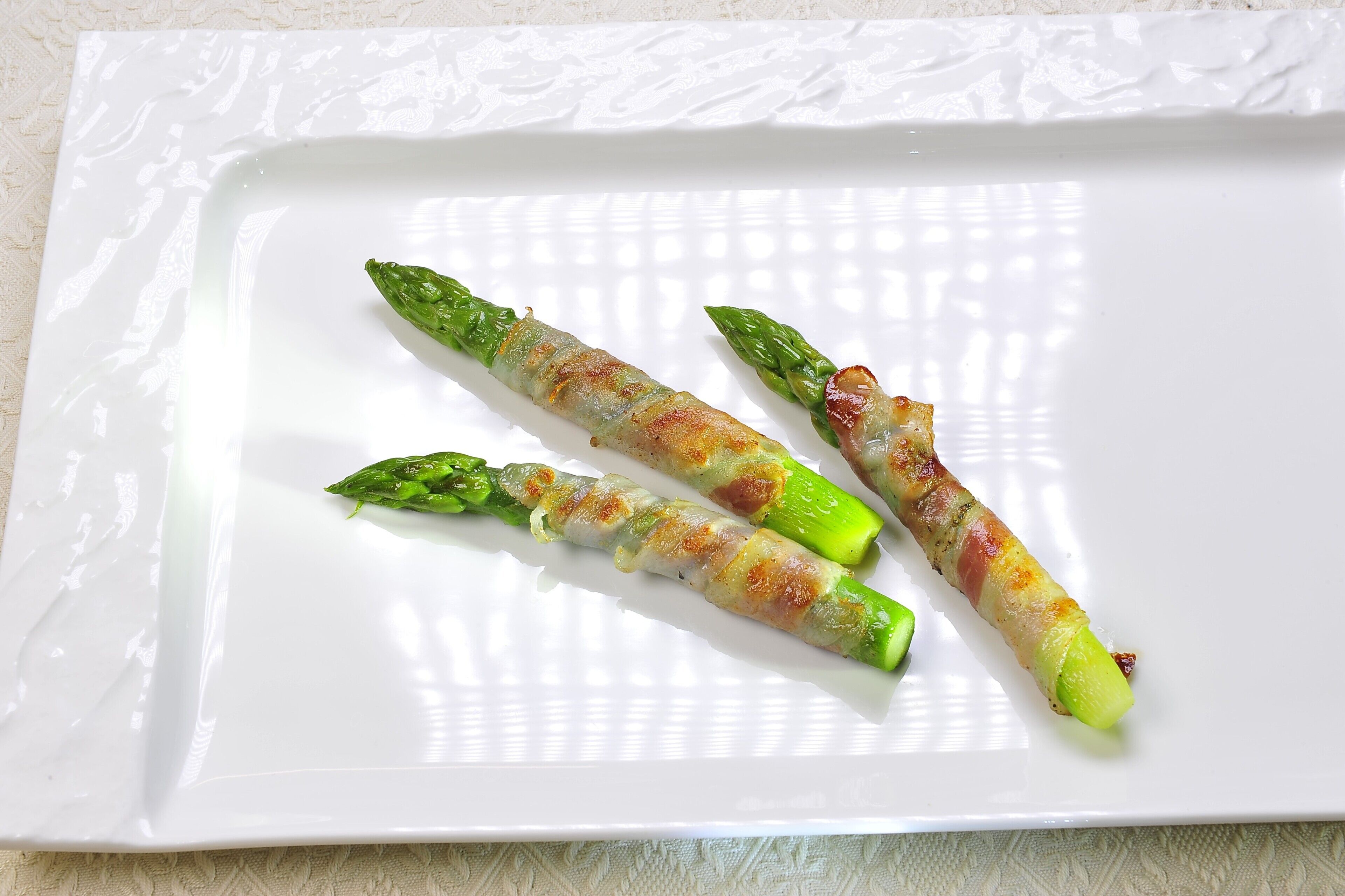 A white plate with three asparagus spears wrapped in bacon.