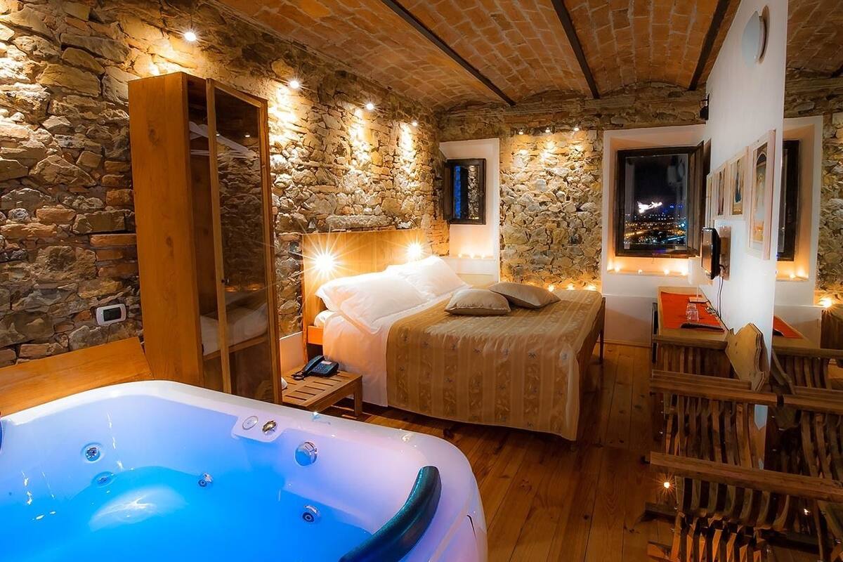 A cozy room with a stone wall, a bed, a wooden cabinet, and a hot tub.