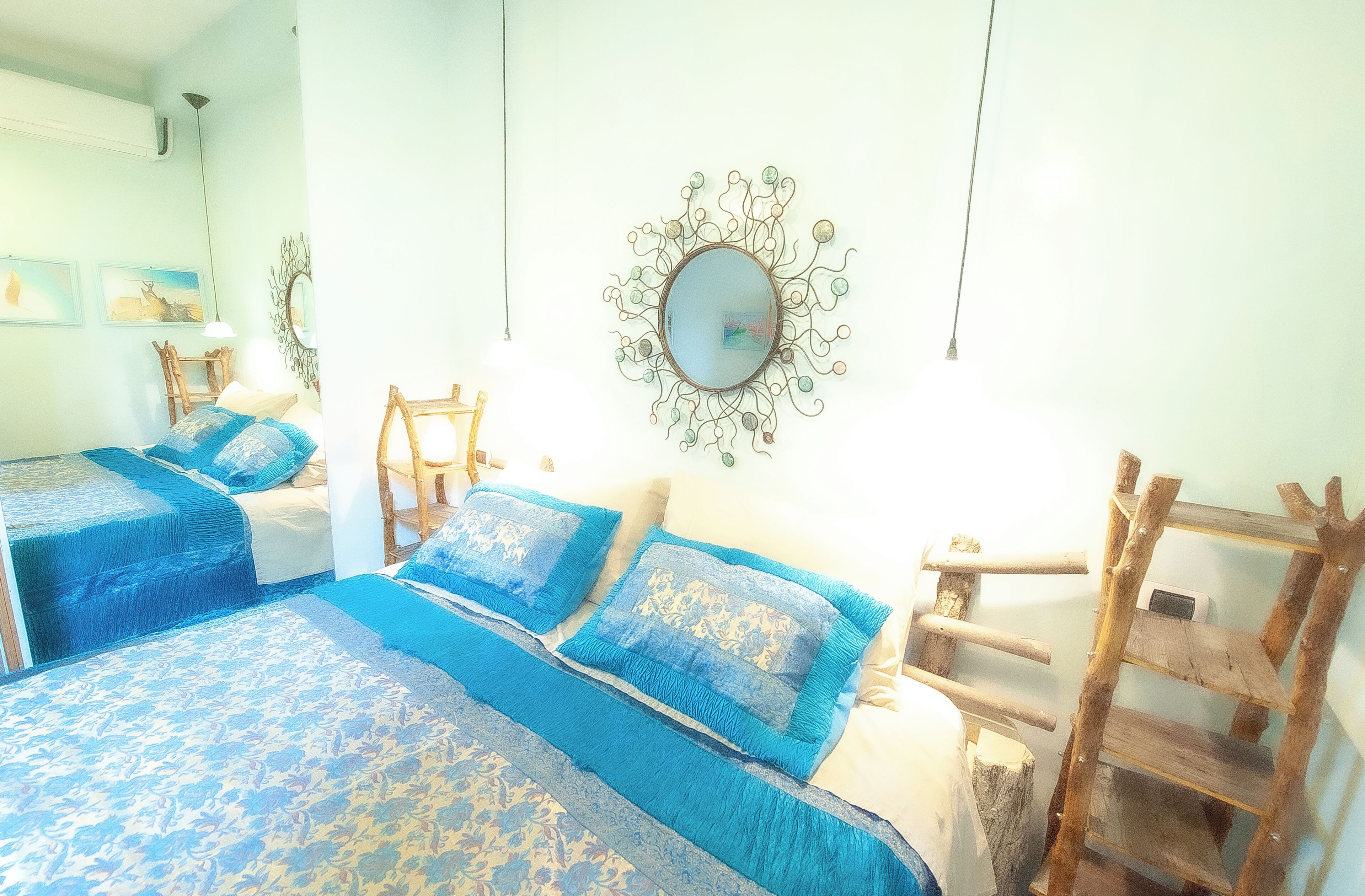 Un dormitorio con dos camas, una estantería de escalera de madera y un espejo montado en la pared.