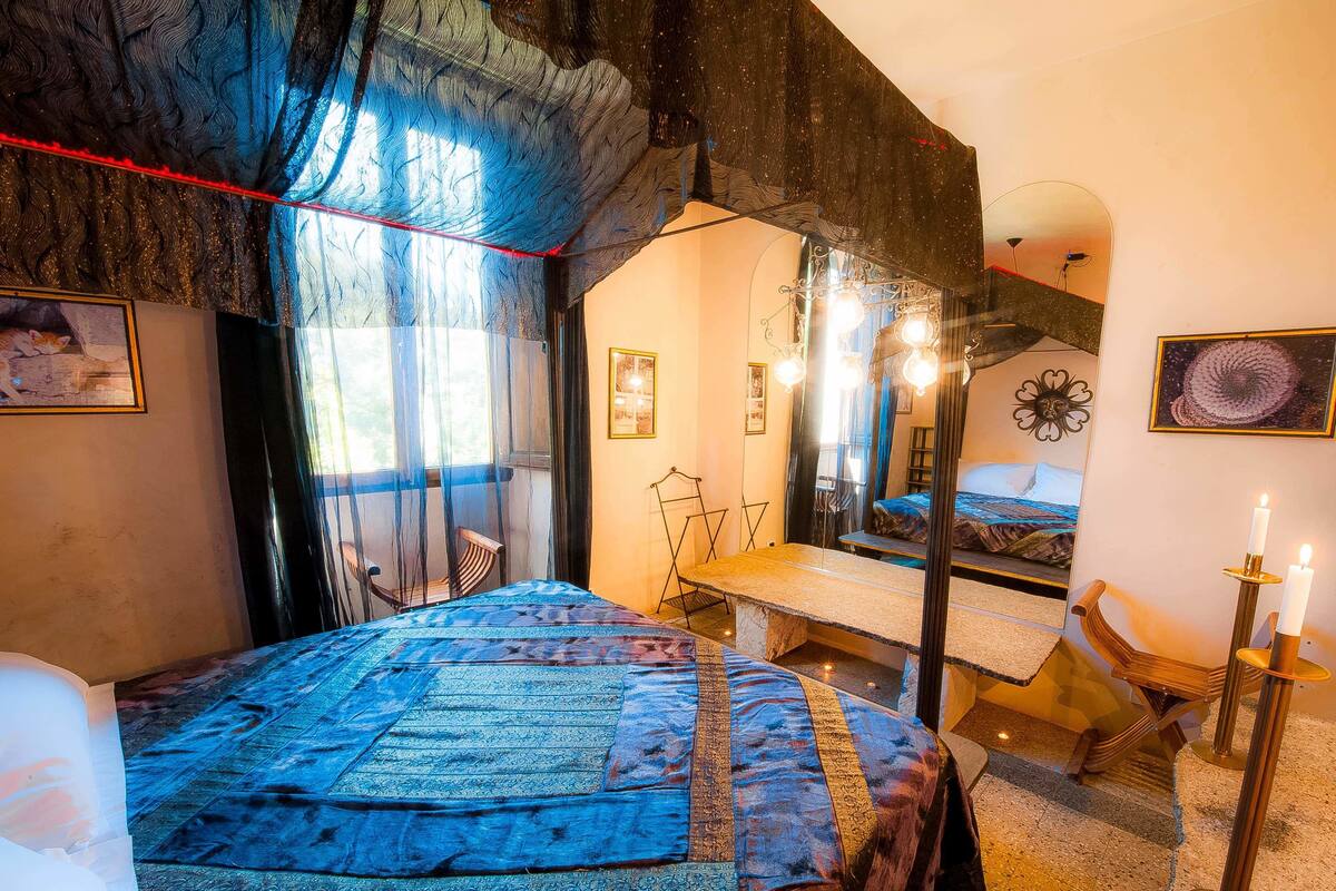 A bedroom with a large bed, a mirror, and a view of a balcony.