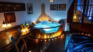 A room with a large, ornate bathtub, a wooden table with a bottle and glasses, and a window with curtains. - Castello di Montalbano (Florence)