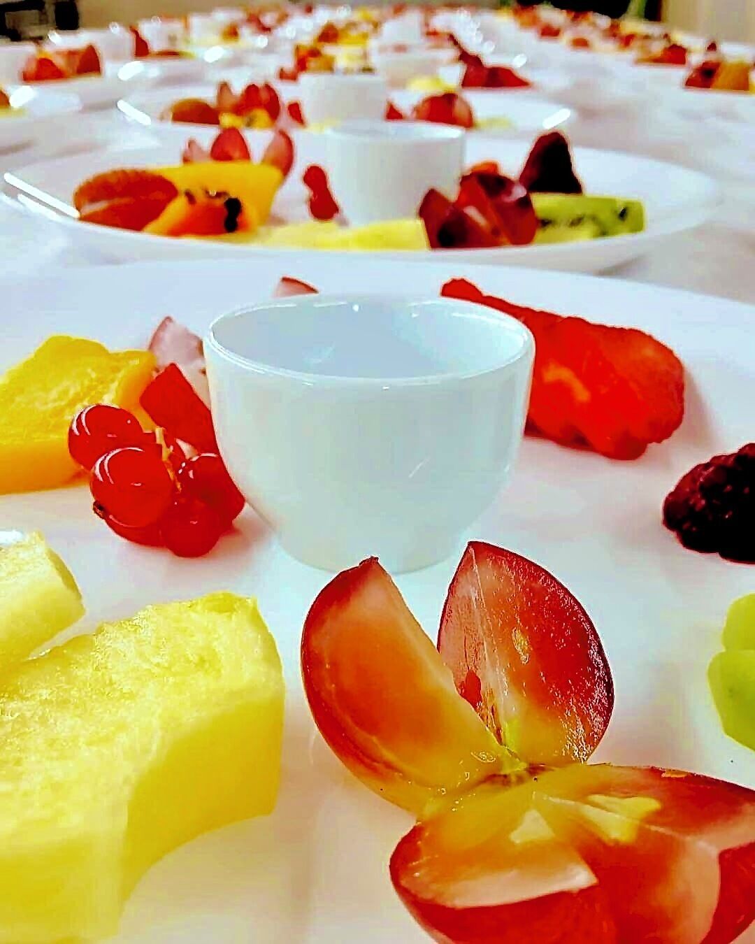 A dessert table with various fruits and a small bowl of white dessert.