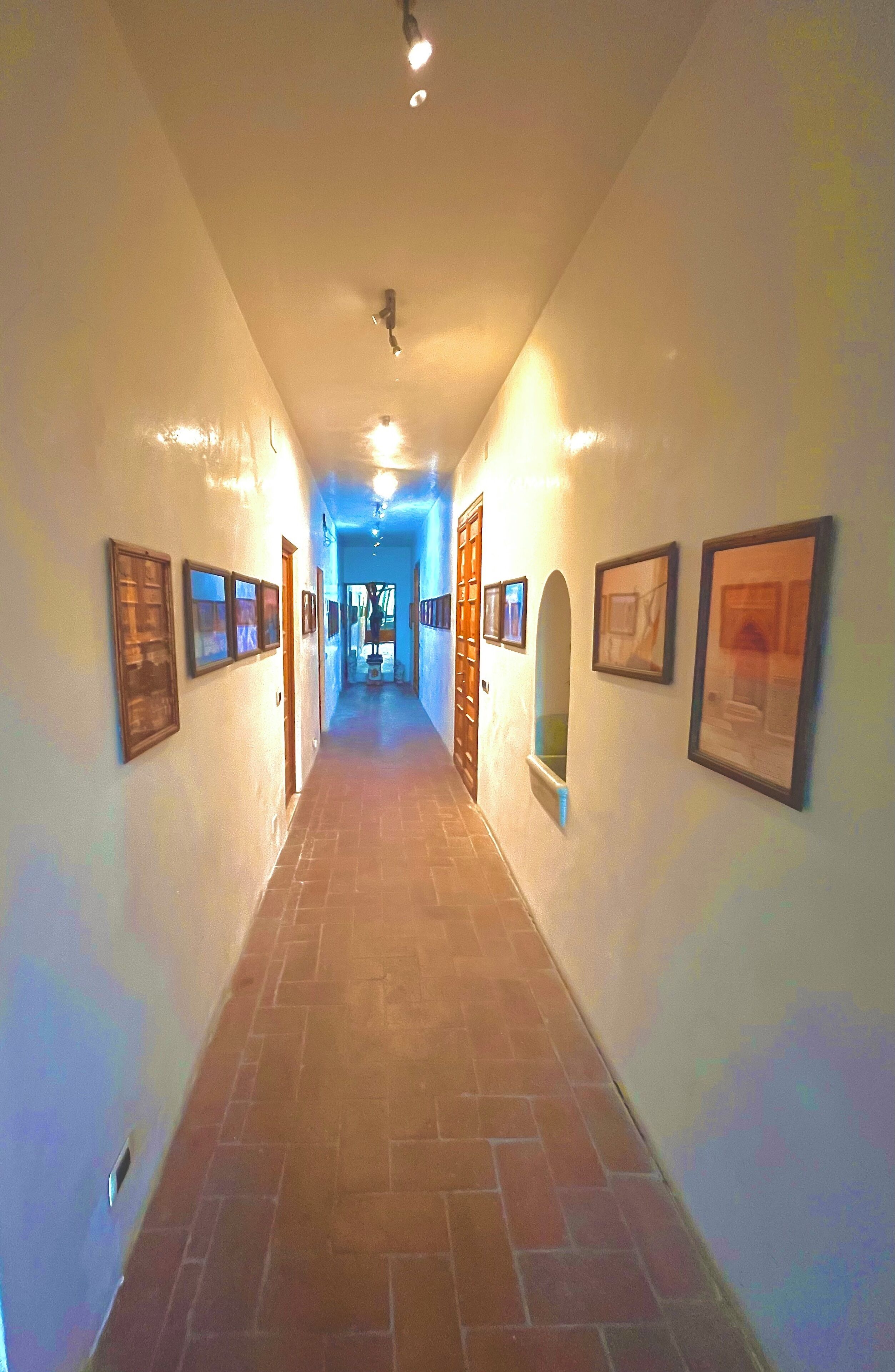 A corridor with framed pictures on the walls, a tiled floor, and a ceiling light.