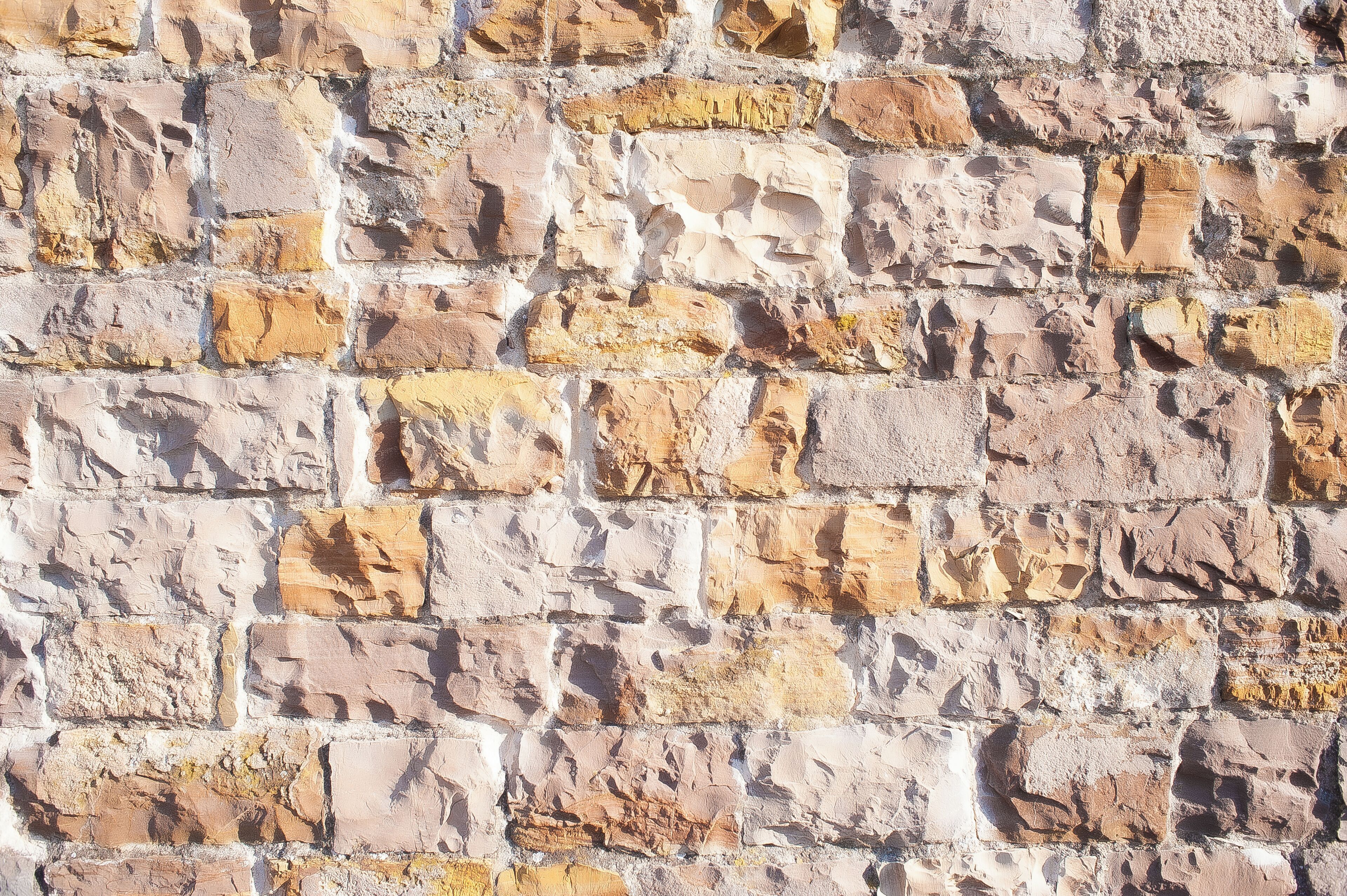 A textured stone wall with irregularly shaped stones in various shades of beige and brown.