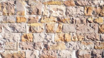A textured stone wall with irregularly shaped stones in various shades of beige and brown.