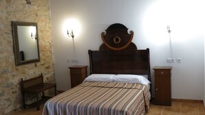 Un dormitorio con una cama de madera, una mesita de noche, un espejo y luces fijadas a la pared.