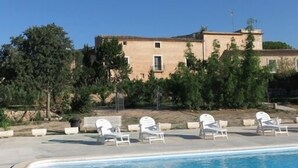 Una piscina con sillas de descanso, un edificio con techo de tejas y árboles al fondo.