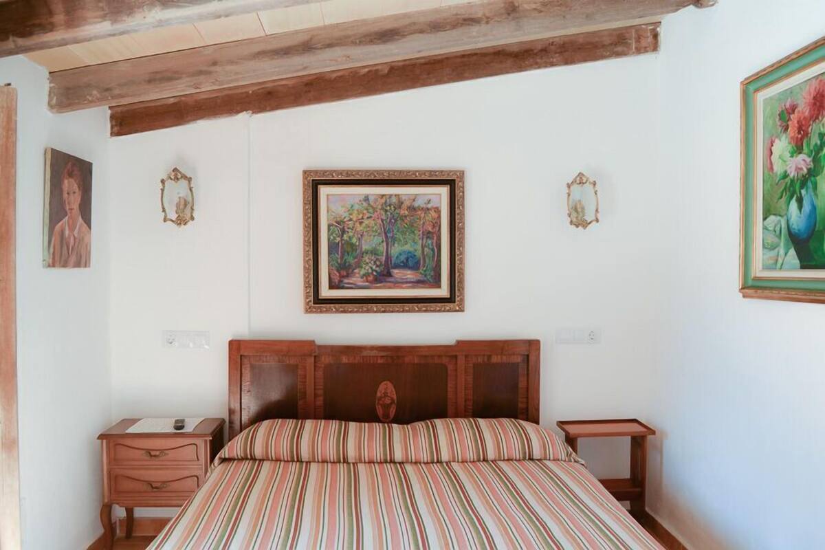 Un dormitorio con cabecera de madera, una cama con ropa de cama a rayas, dos mesitas de noche y cuadros en las paredes.