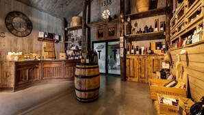Un intérieur rustique, avec des meubles en bois, une grande horloge et des étagères où sont exposées diverses bouteilles et paniers.