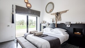 Une chambre à coucher moderne avec un grand lit, un banc, une cheminée et une vue sur l’extérieur.