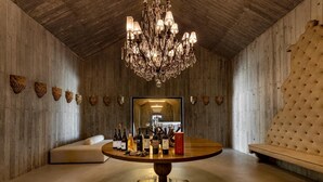 Une pièce avec un plafond en bois, une table ronde sur laquelle sont posées des bouteilles, un canapé et un grand miroir qui reflète une partie de la cuisine.