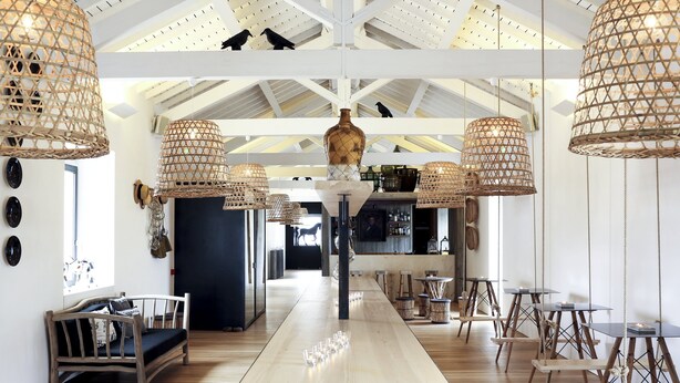 Une pièce spacieuse avec une longue table en bois, des lampes suspendues en osier et un banc en bois rustique.