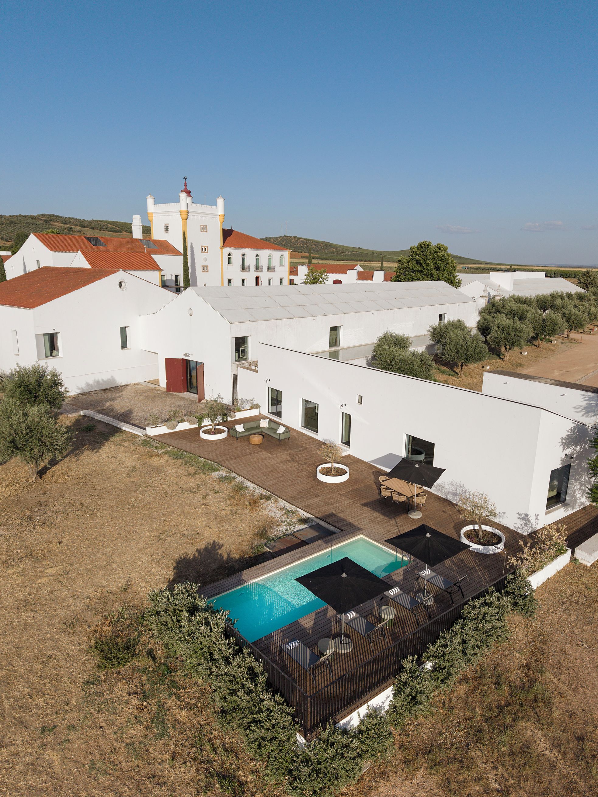 Zona residencial con piscina, mobiliario exterior y un edificio grande de color blanco con techo rojo.