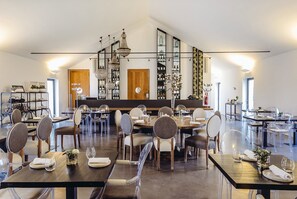 Un restaurante espacioso con numerosas mesas y sillas, una zona de bar central y varios candelabros colgantes.